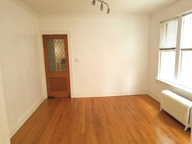 spare room with radiator, light wood-type flooring, baseboards, and ornamental molding