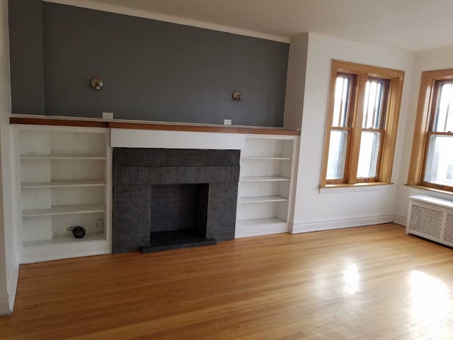 unfurnished living room with built in shelves, radiator heating unit, a brick fireplace, wood finished floors, and baseboards