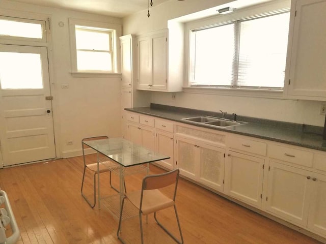 kitchen with dark countertops, light wood-type flooring, a sink, and white cabinets