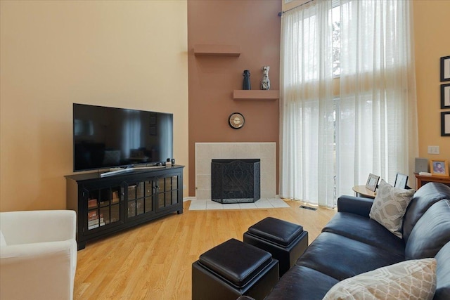 living room with a tiled fireplace and light wood-type flooring