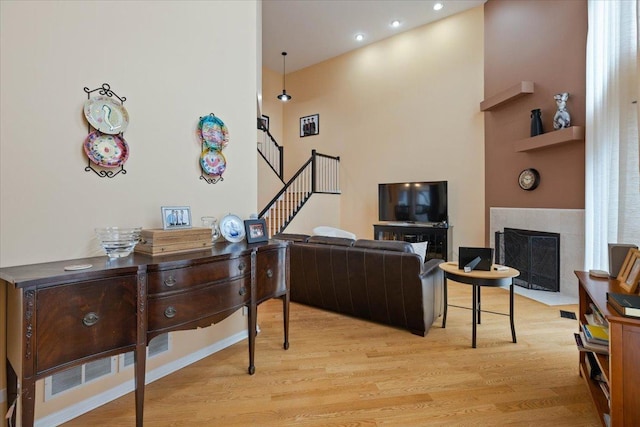 living room featuring a tiled fireplace, a towering ceiling, and light hardwood / wood-style flooring