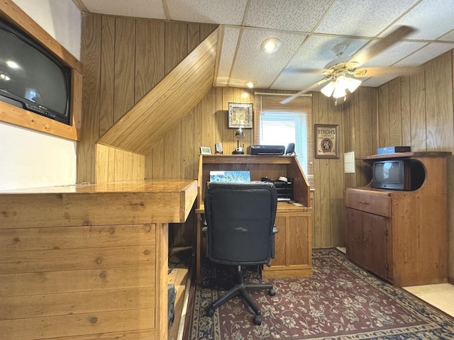 home office featuring ceiling fan, a paneled ceiling, and wooden walls