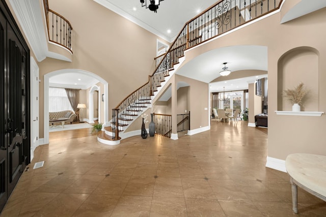 foyer entrance featuring arched walkways, a notable chandelier, ornamental molding, baseboards, and stairs