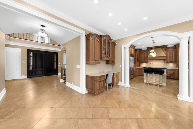 entrance foyer featuring ornamental molding, arched walkways, decorative columns, and baseboards