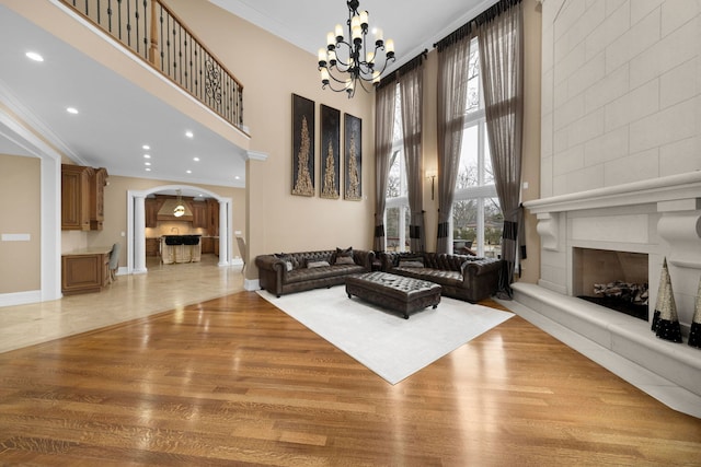 living room featuring arched walkways, a large fireplace, ornamental molding, and a towering ceiling