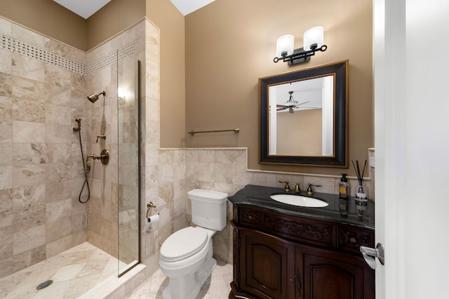 full bath featuring tile walls, toilet, wainscoting, vanity, and tiled shower