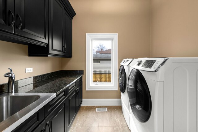 washroom with a sink, visible vents, baseboards, cabinet space, and washing machine and clothes dryer