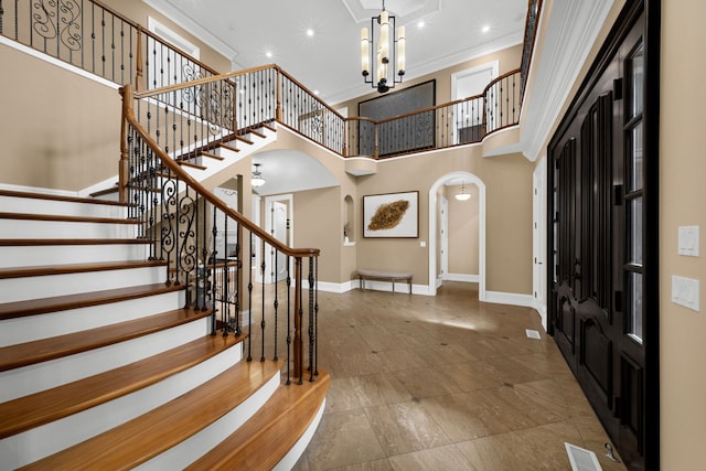 foyer with baseboards, visible vents, arched walkways, a towering ceiling, and crown molding