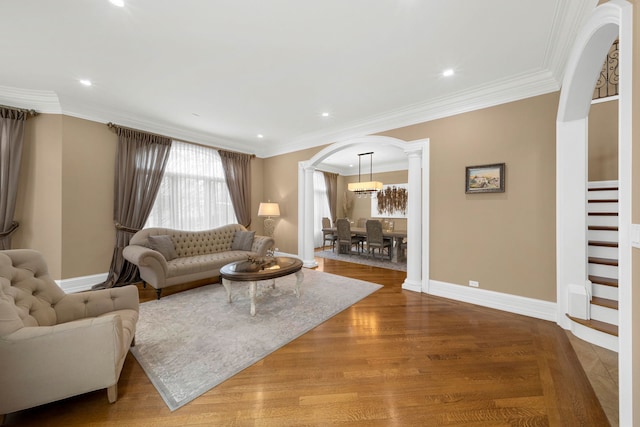 living room featuring arched walkways, wood finished floors, baseboards, ornamental molding, and stairway