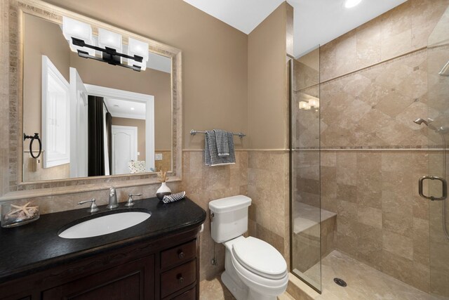 bathroom with toilet, a wainscoted wall, vanity, tile walls, and a shower stall