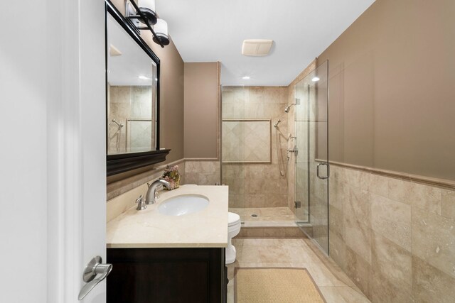 full bathroom featuring toilet, vanity, tile walls, a shower stall, and tile patterned floors