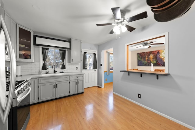 kitchen featuring sink, appliances with stainless steel finishes, gray cabinets, light hardwood / wood-style floors, and decorative backsplash