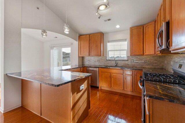 kitchen featuring lofted ceiling, appliances with stainless steel finishes, kitchen peninsula, pendant lighting, and dark stone counters