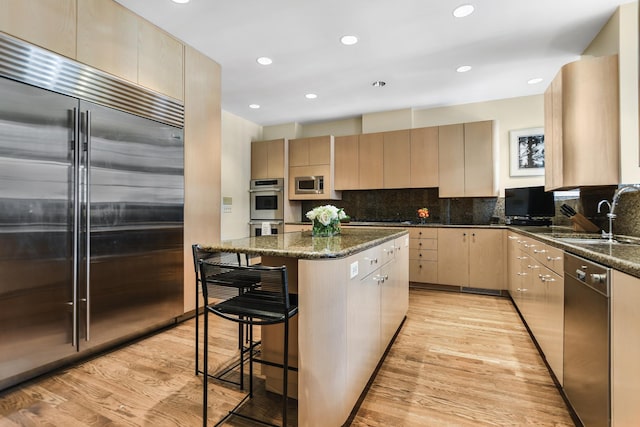 kitchen featuring sink, a center island, built in appliances, and dark stone counters