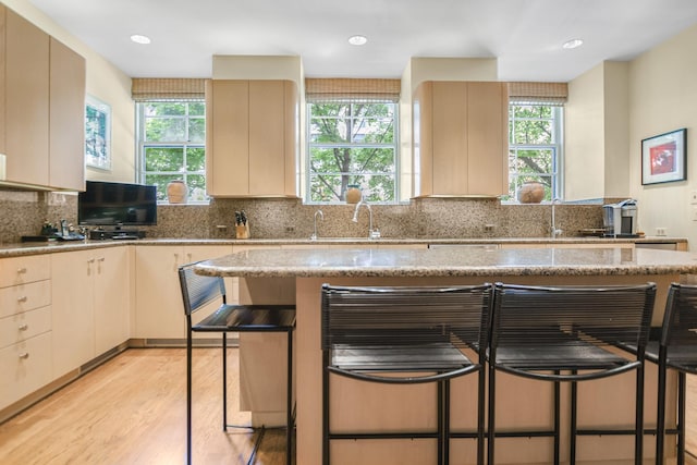 kitchen with cream cabinets, a breakfast bar, decorative backsplash, and light hardwood / wood-style flooring