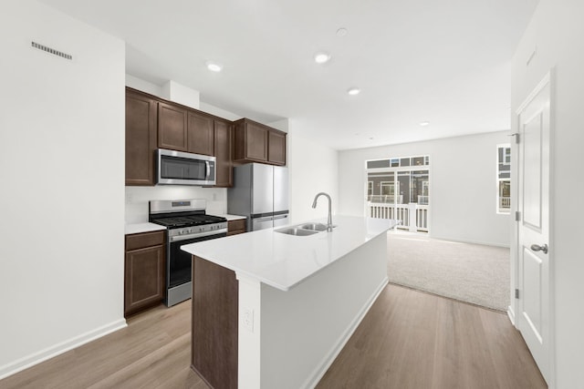 kitchen featuring sink, a kitchen island with sink, stainless steel appliances, dark brown cabinets, and light hardwood / wood-style flooring