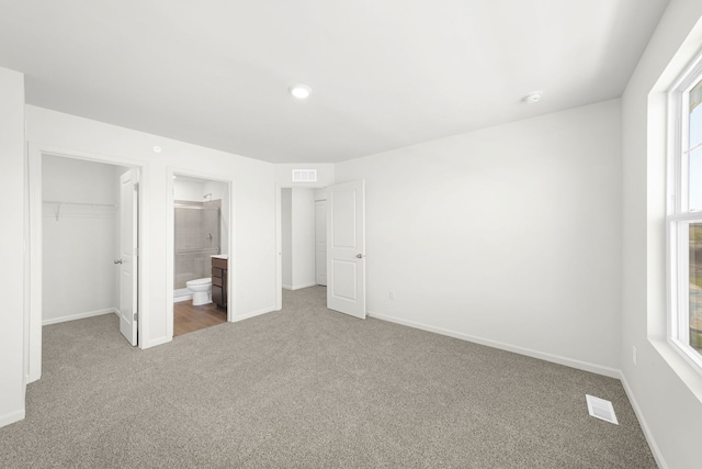 unfurnished bedroom with a walk in closet, ensuite bathroom, carpet floors, and a closet