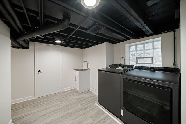 clothes washing area featuring washing machine and clothes dryer, sink, and light hardwood / wood-style floors