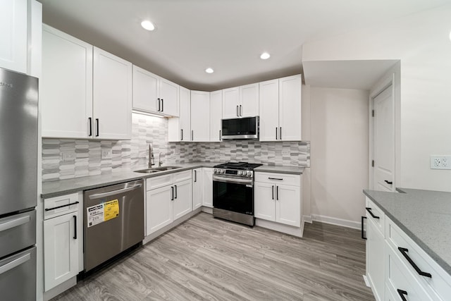 kitchen featuring white cabinetry, sink, stainless steel appliances, light stone countertops, and light wood-type flooring