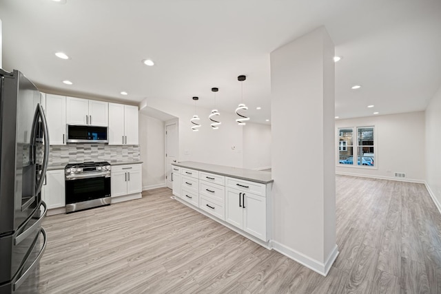 kitchen featuring tasteful backsplash, hanging light fixtures, light wood-type flooring, appliances with stainless steel finishes, and white cabinets