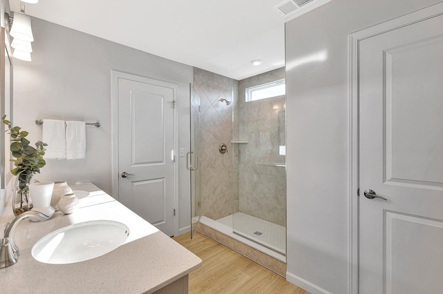 full bath featuring a shower stall, wood finished floors, vanity, baseboards, and visible vents