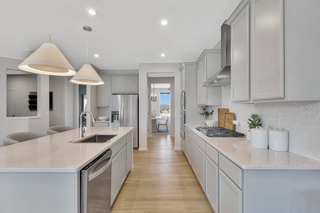 kitchen with wall chimney range hood, gray cabinets, a sink, decorative backsplash, and appliances with stainless steel finishes
