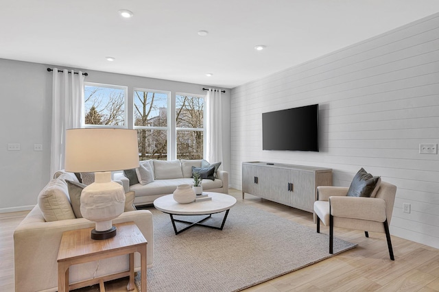 living room with recessed lighting, light wood-style floors, and wood walls