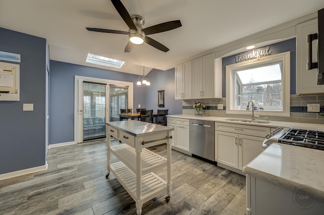 kitchen with pendant lighting, sink, white cabinets, stainless steel dishwasher, and light hardwood / wood-style floors