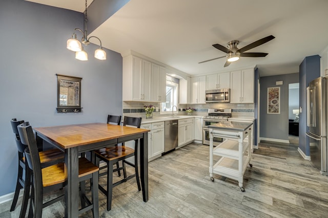 kitchen with pendant lighting, sink, backsplash, stainless steel appliances, and white cabinets