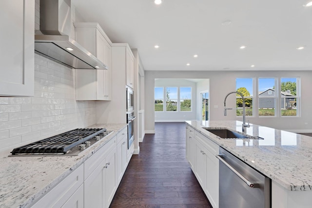 kitchen with a spacious island, wall chimney exhaust hood, sink, light stone counters, and stainless steel appliances