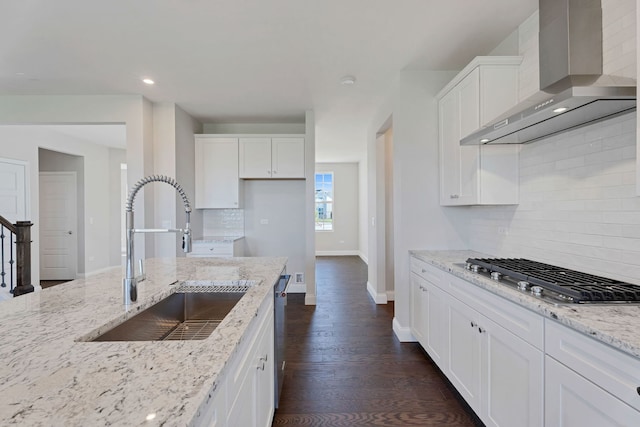 kitchen with sink, white cabinets, stainless steel appliances, light stone countertops, and wall chimney range hood