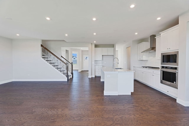 kitchen with white cabinets, appliances with stainless steel finishes, a center island with sink, and wall chimney range hood