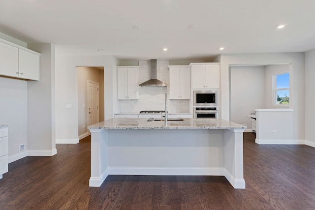 kitchen featuring stainless steel appliances, white cabinetry, a center island with sink, and wall chimney exhaust hood