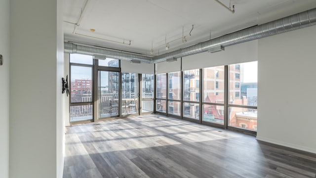 spare room with floor to ceiling windows, wood finished floors, rail lighting, and a healthy amount of sunlight