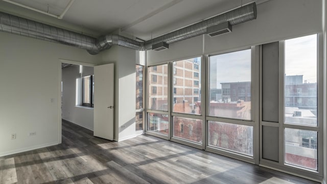 spare room featuring baseboards, visible vents, a sunroom, wood finished floors, and a view of city