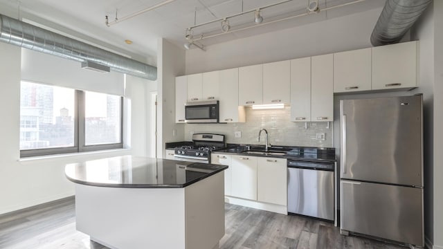 kitchen featuring a center island, stainless steel appliances, tasteful backsplash, a sink, and wood finished floors