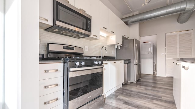 kitchen with appliances with stainless steel finishes, white cabinetry, backsplash, and wood finished floors