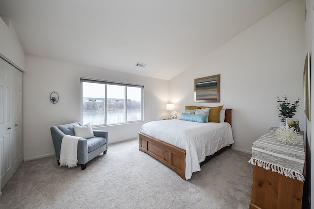 bedroom featuring a water view, a closet, vaulted ceiling, and light carpet