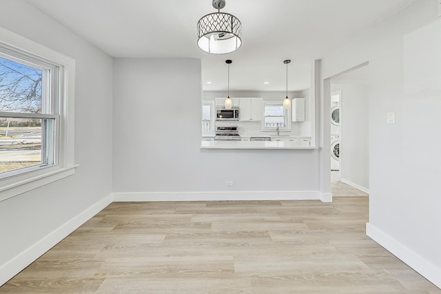 kitchen with stacked washer and dryer, stove, hanging light fixtures, white cabinets, and light wood-type flooring