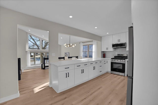 kitchen featuring appliances with stainless steel finishes, white cabinetry, a chandelier, hanging light fixtures, and light hardwood / wood-style floors