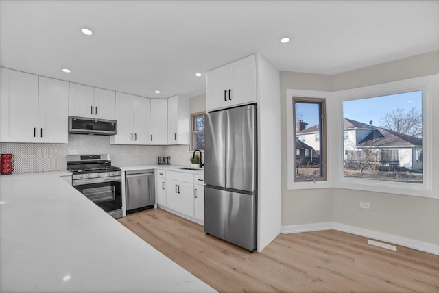 kitchen featuring sink, appliances with stainless steel finishes, white cabinetry, tasteful backsplash, and light wood-type flooring