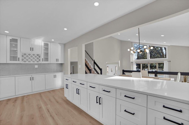 kitchen featuring white cabinetry, backsplash, hanging light fixtures, a notable chandelier, and light wood-type flooring