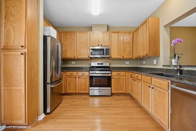 kitchen with appliances with stainless steel finishes, light hardwood / wood-style floors, sink, and dark stone counters