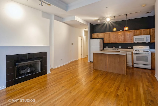 kitchen with decorative light fixtures, a tiled fireplace, a center island, white appliances, and light hardwood / wood-style flooring