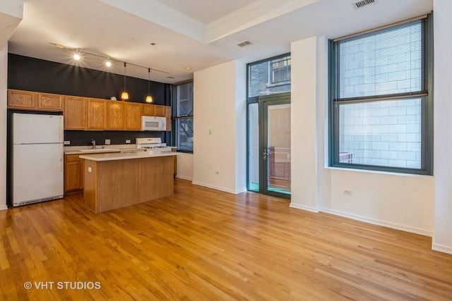 kitchen with white appliances, a kitchen island, hanging light fixtures, and light hardwood / wood-style flooring