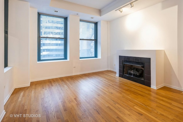 unfurnished living room featuring a tile fireplace, track lighting, and light hardwood / wood-style flooring