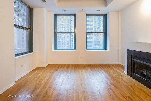 unfurnished living room featuring light hardwood / wood-style flooring, a fireplace, and a tray ceiling