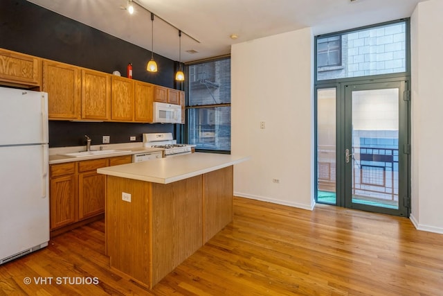 kitchen with sink, white appliances, light hardwood / wood-style flooring, hanging light fixtures, and a kitchen island