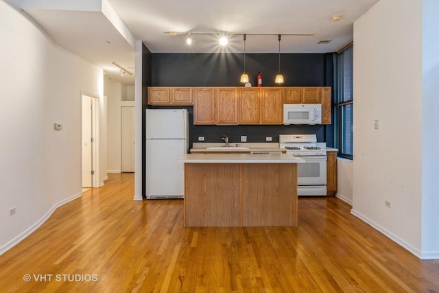 kitchen with sink, light hardwood / wood-style flooring, pendant lighting, white appliances, and a kitchen island with sink