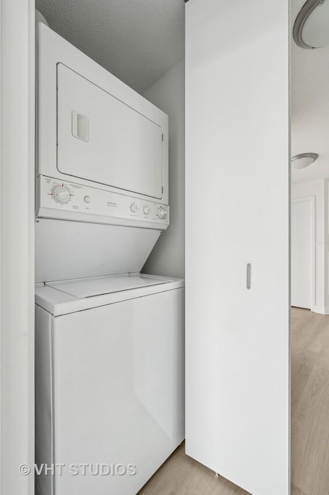 laundry room featuring light wood-type flooring, a textured ceiling, and stacked washing maching and dryer